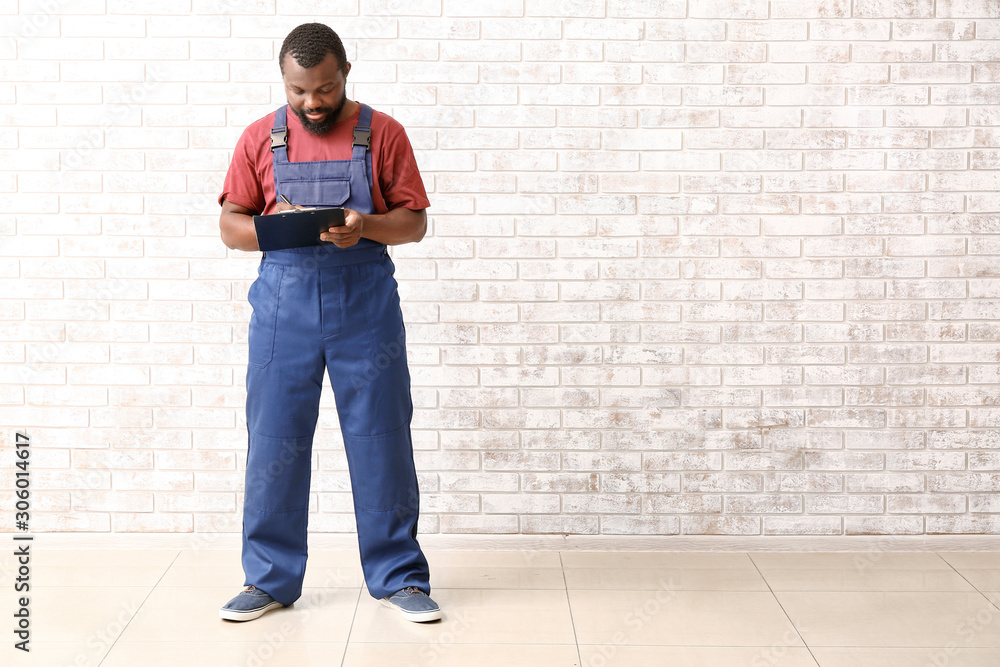 African-American car mechanic with clipboard near brick wall