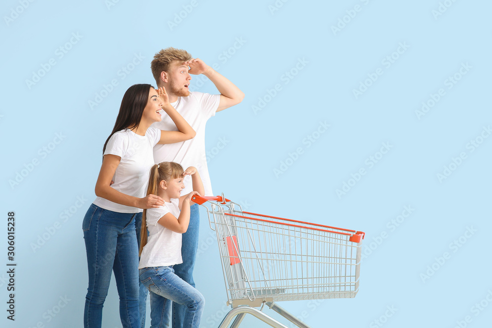 Family with empty shopping cart on color background