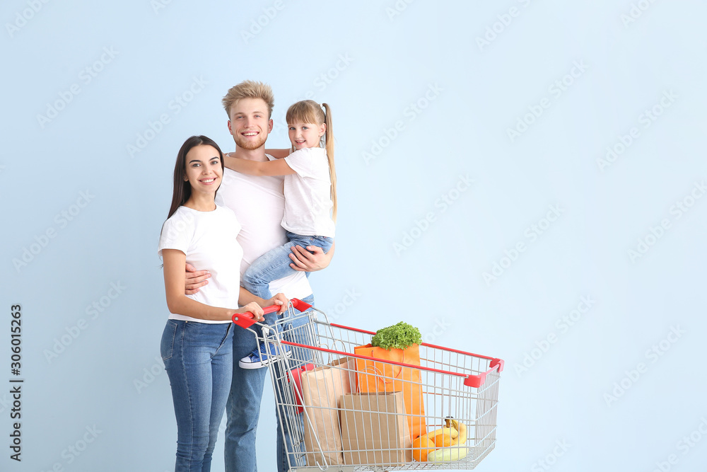 Family with shopping cart on color background