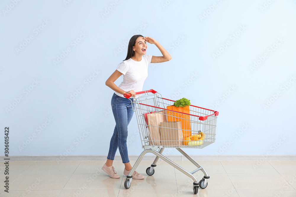 Young woman with shopping cart near color wall