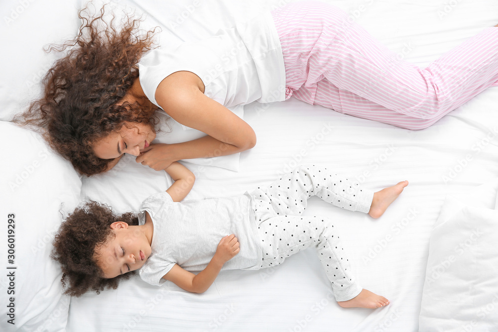 Little African-American girl with mother sleeping in bed