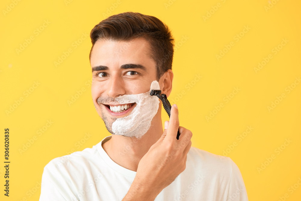 Handsome young man shaving against on color background