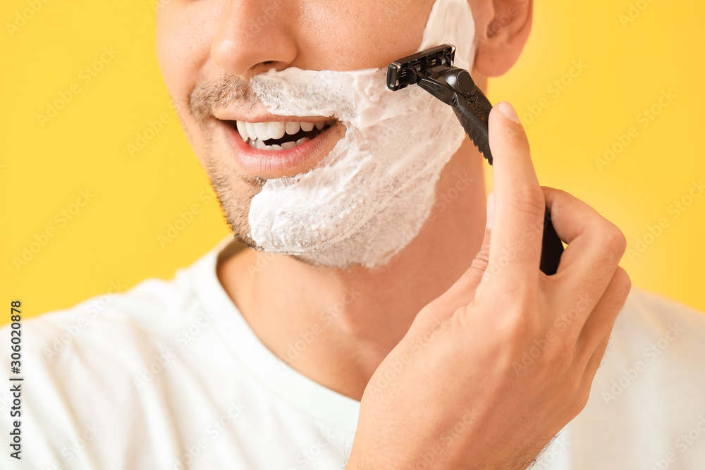 Handsome young man shaving against on color background, closeup