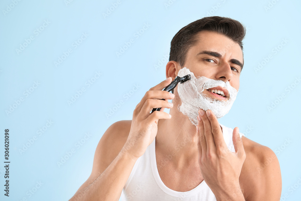 Handsome young man shaving against on color background