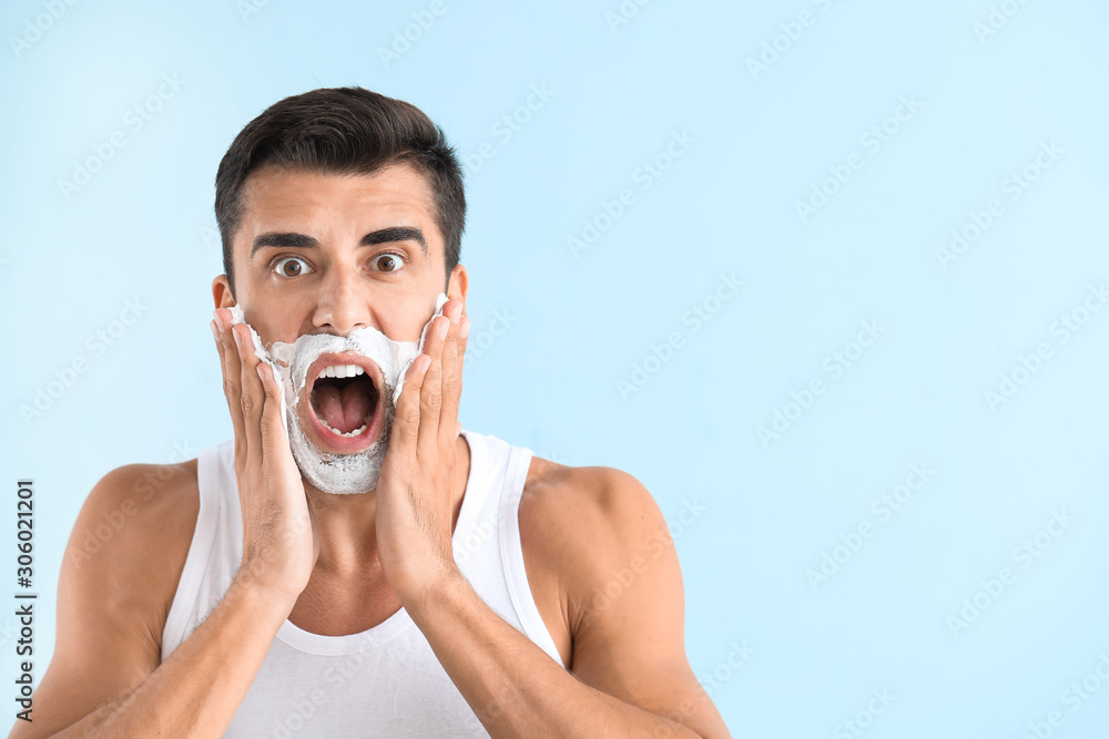 Screaming young man with shaving foam on his face against color background