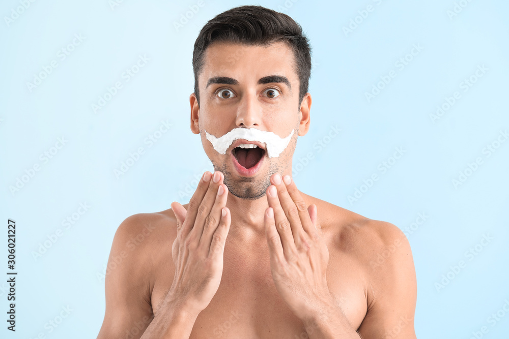 Surprised young man with shaving foam on his face against color background