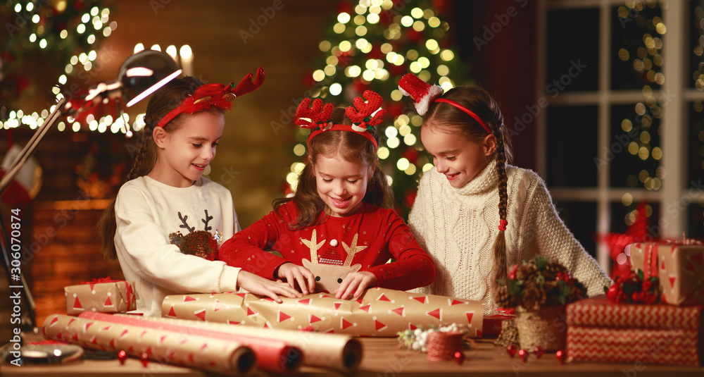 happy funny children girls pack Christmas gifts at evening in home.