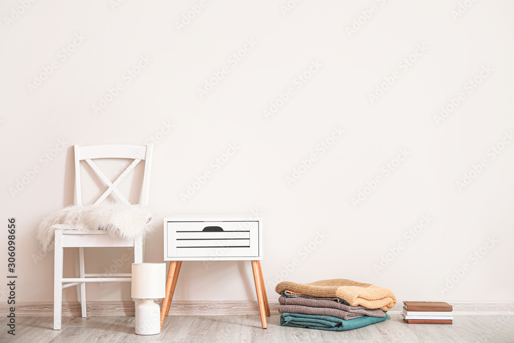 Chair with table, plaids, books and lamp near white wall