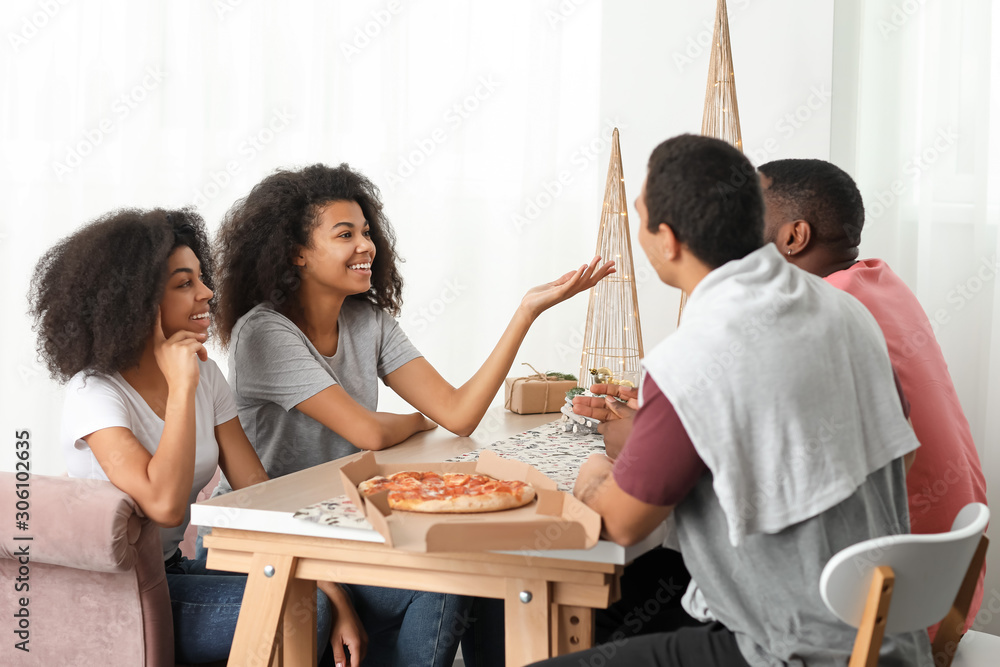 Young African-American friends eating tasty pizza at home