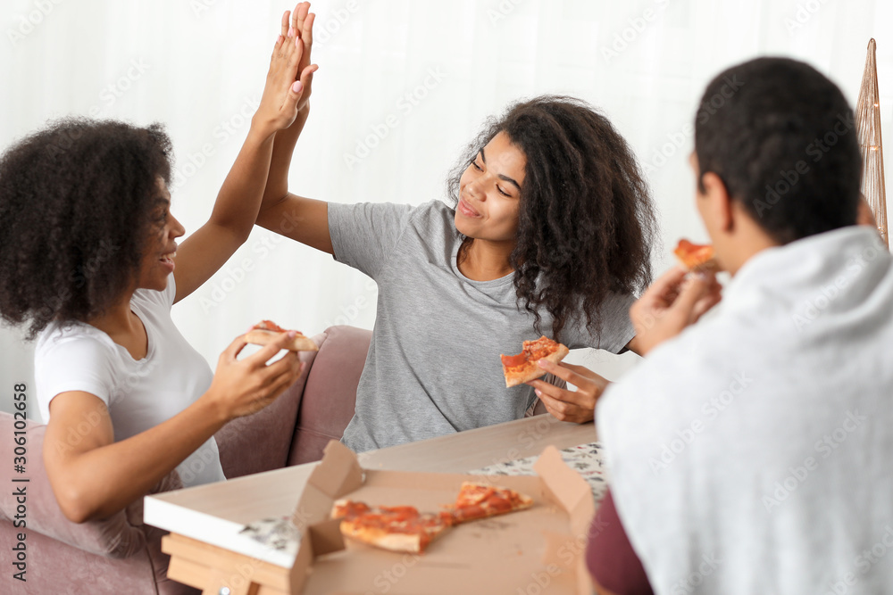 Young African-American friends eating tasty pizza at home