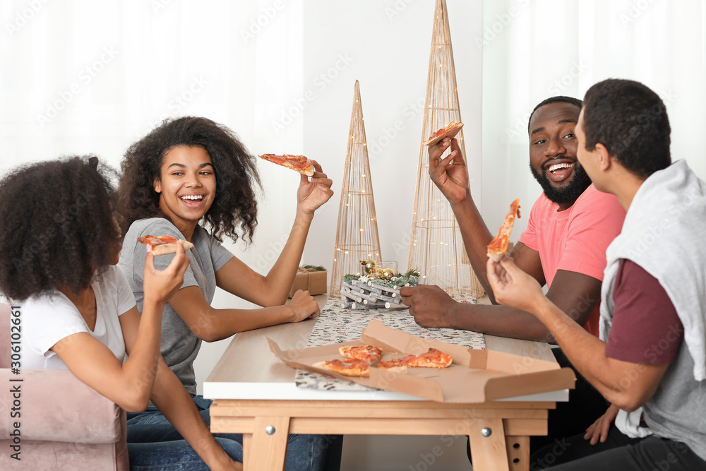 Young African-American friends eating tasty pizza at home