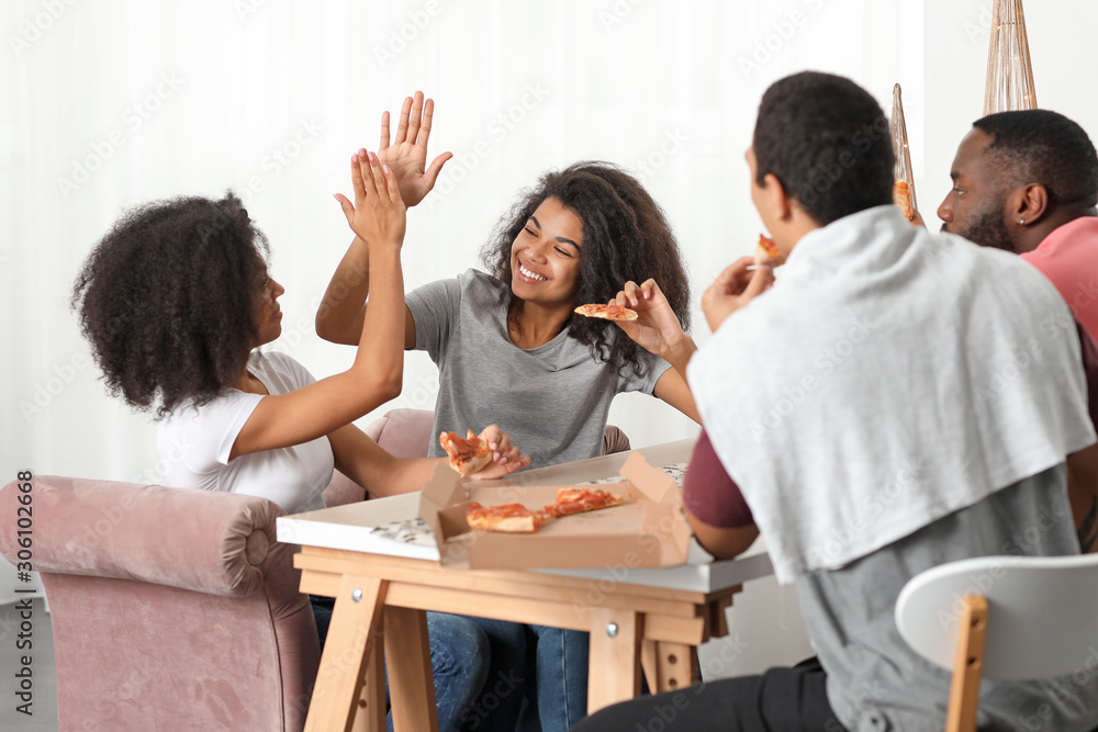 Young African-American friends eating tasty pizza at home