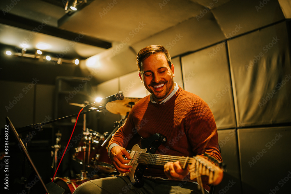 Portrait of a handsome smiling man playing electric guitar in recording studio.