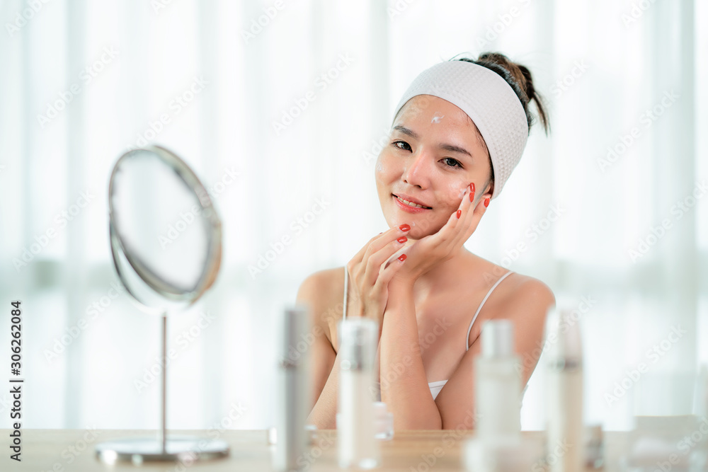 Portrait of beautiful Asian young woman caring of her skin sitting near mirror in bedroom with skin 