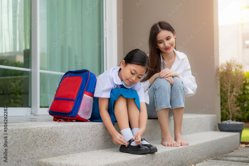 Asian mother watching her daughter preschool students in uniform  to wearing their own shoes infront