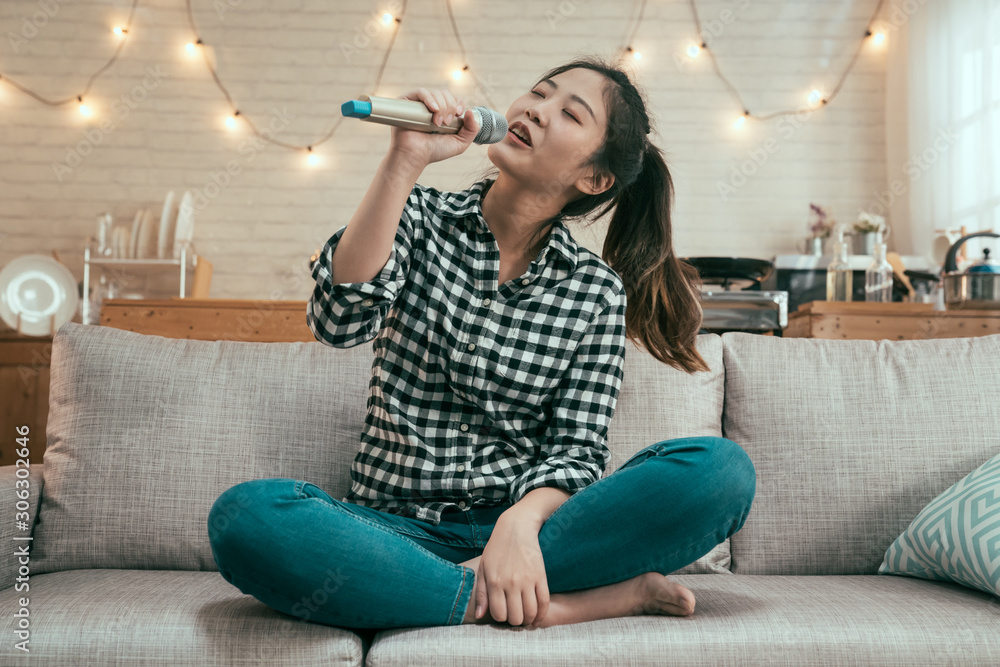 young asian girl singing with microphone on sofa at home kitchen. beautiful lady love music enjoy ka