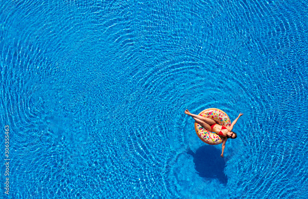 Aerial view of a woman in red bikini lying on a donut in the pool