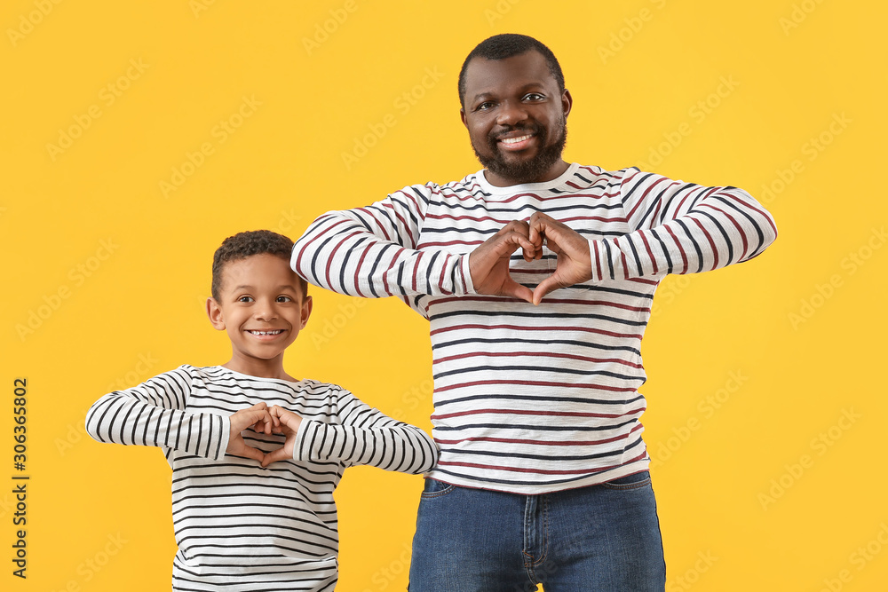 Portrait of African-American man and his little son making hearts with their hands on color backgrou