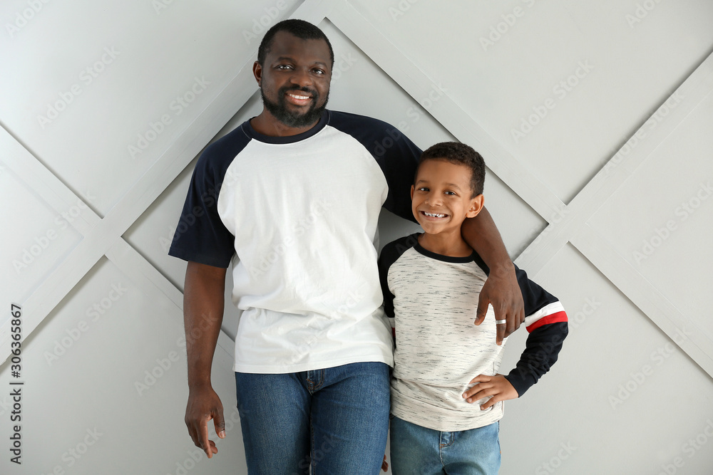 Portrait of African-American man with his little son on light background