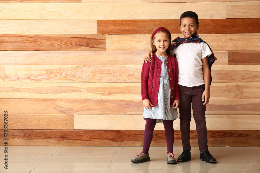 Fashionable little children in autumn clothes near wooden wall