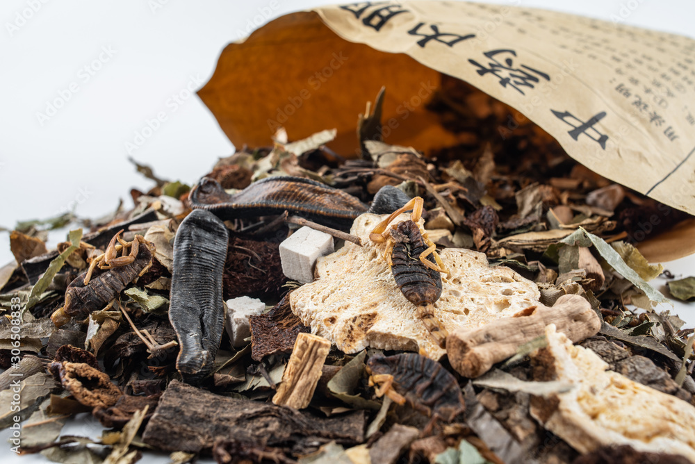 Chinese medicinal herbs pouring out of a paper bag on white background