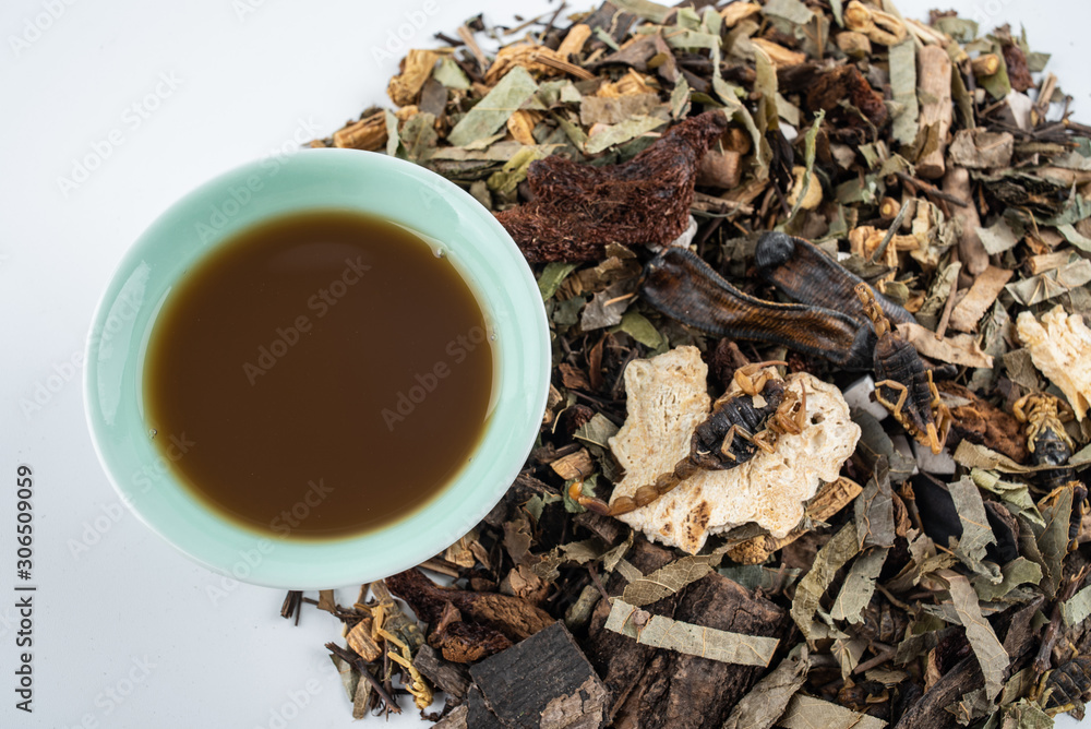 A pile of Chinese herbs and a bowl of boiled medicinal soup on white background