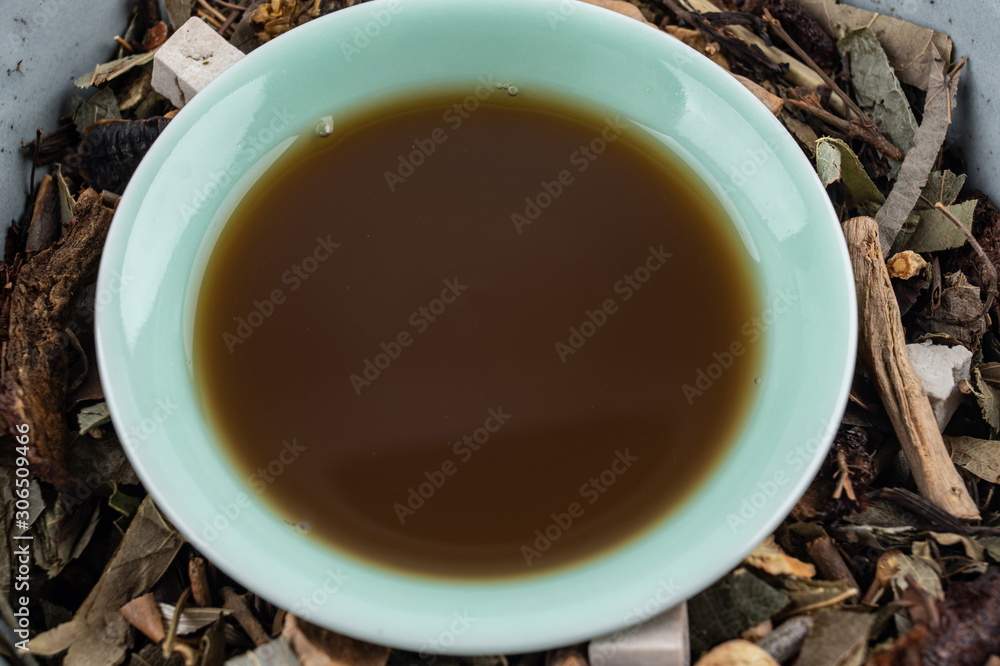 A pile of Chinese herbs and a bowl of boiled medicinal soup on white background