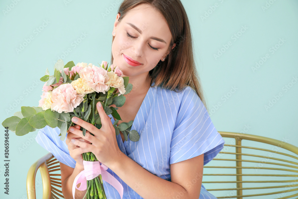 Beautiful young woman with bouquet of carnation flowers sitting in armchair on color background