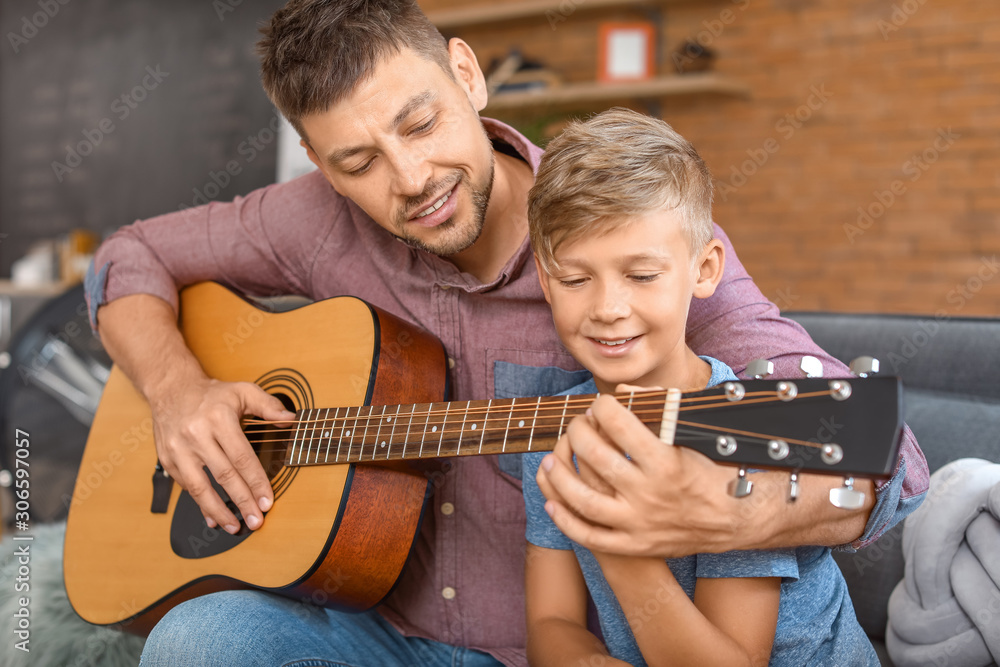 Father teaching his little son to play guitar at home