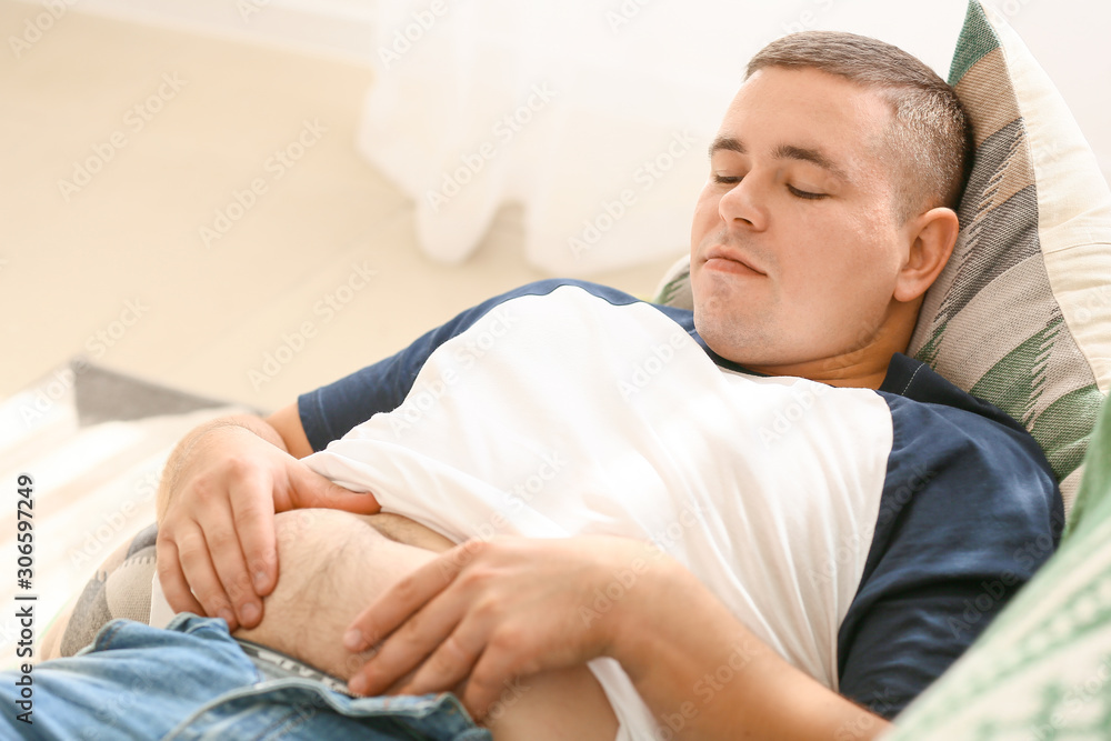 Overweight man lying on sofa at home