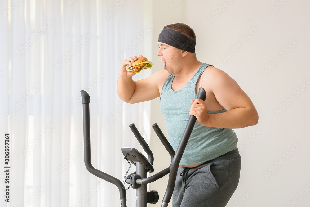 Overweight man eating burger while training at home. Weight loss concept