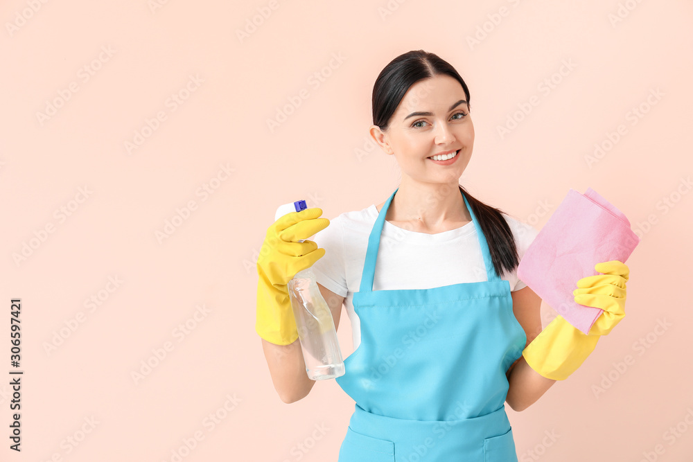 Female janitor with cleaning supplies on color background