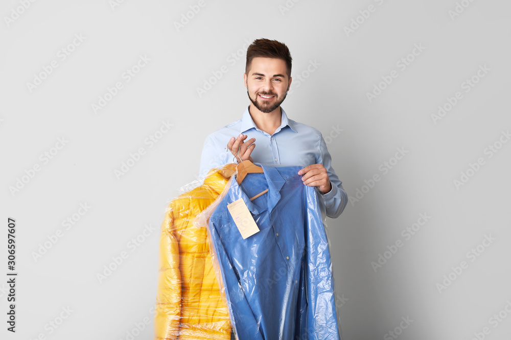 Male worker of modern dry-cleaner with clothes on light background