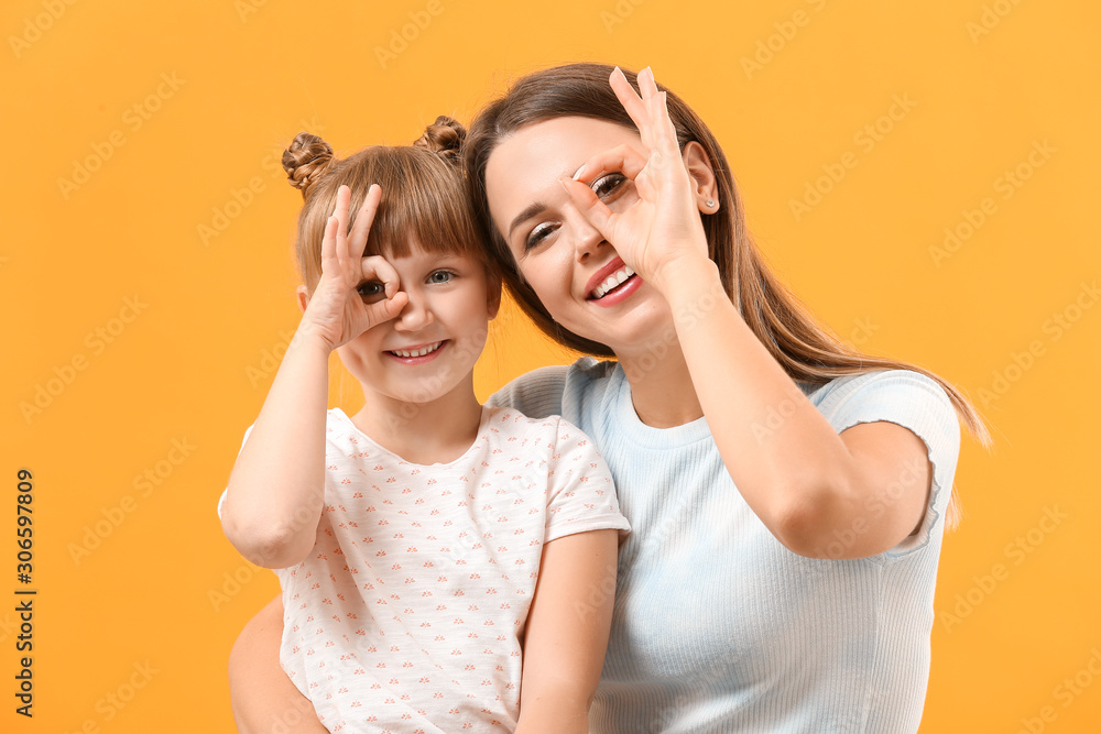 Portrait of happy mother and daughter showing OK gesture on color background