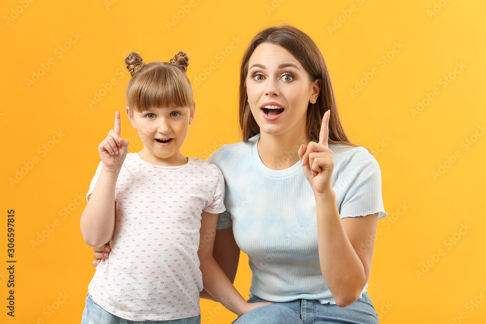 Portrait of emotional mother and daughter with raised index fingers on color background