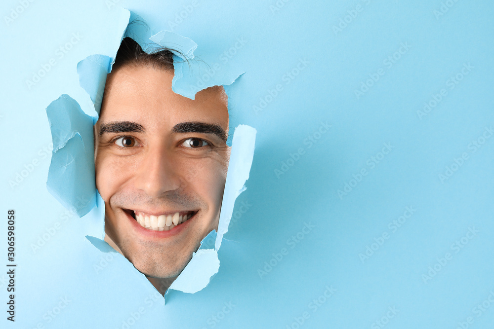 Handsome shaved young man looking out of hole in color paper