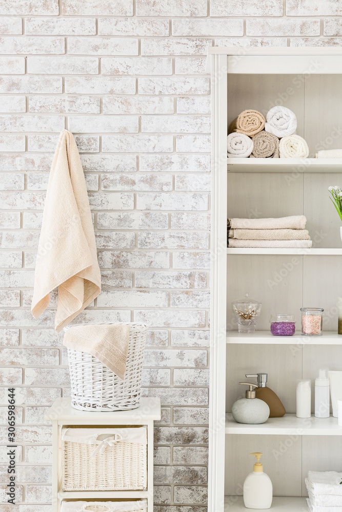 Shelf unit with towels and cosmetics near brick wall in bathroom