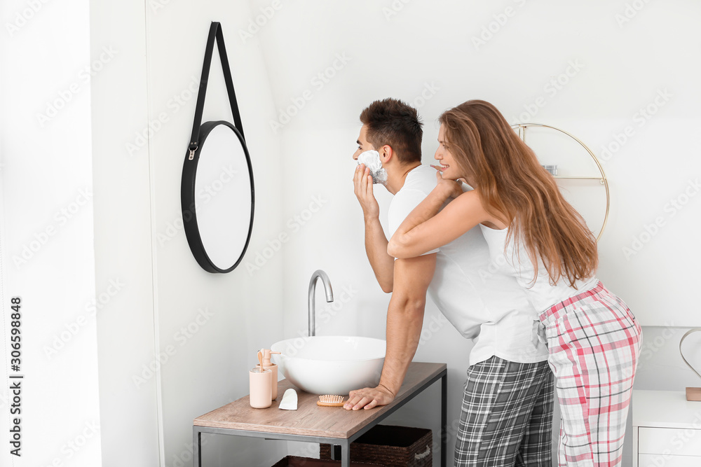 Morning of beautiful young woman and her husband with shaving foam on his face in bathroom