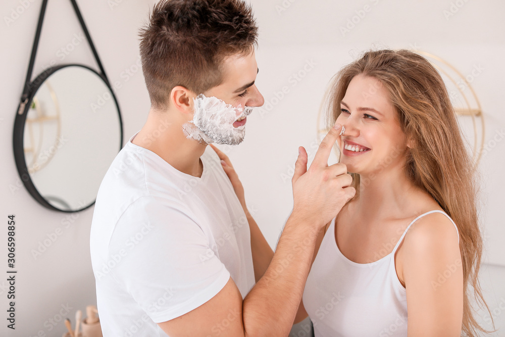 Morning of beautiful young woman and her husband with shaving foam on his face in bathroom