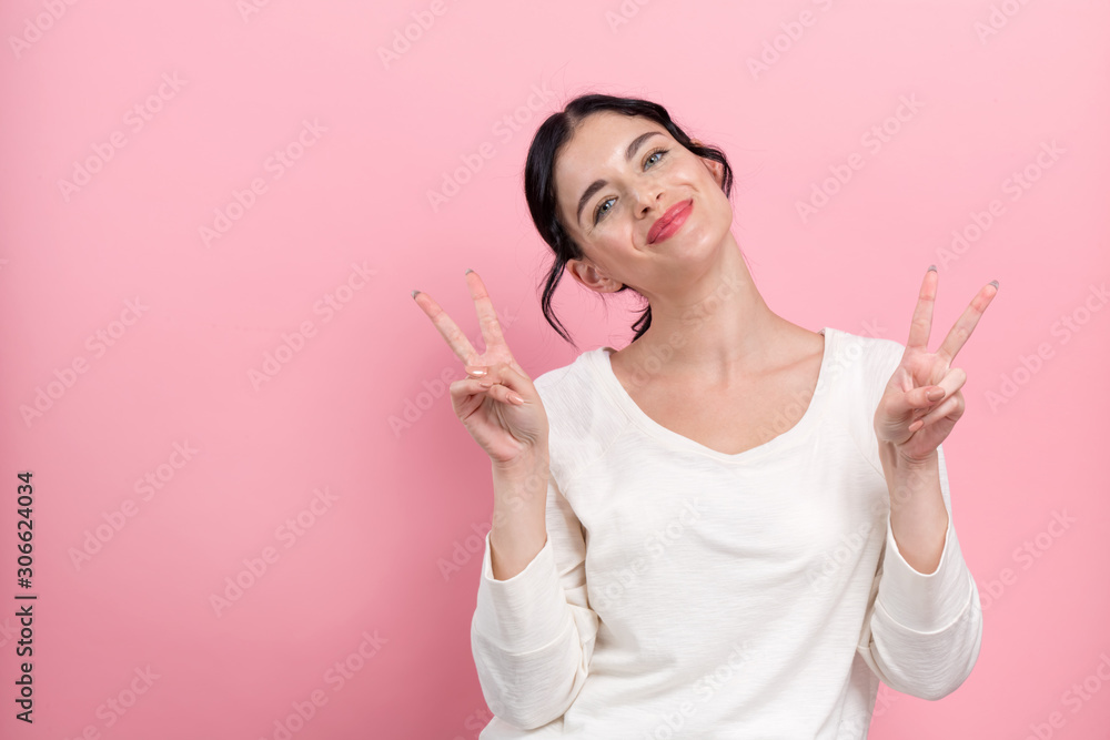 Young woman giving the peace sign on a pink background