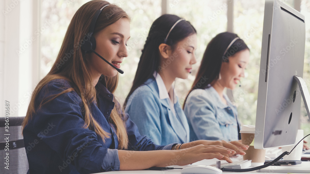 Customer support agent or call center with headset works on desktop computer while supporting the cu