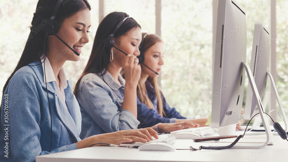 Customer support agent or call center with headset works on desktop computer while supporting the cu