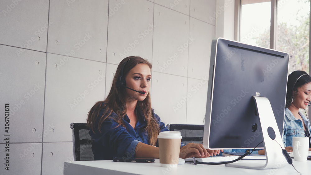 Customer support agent or call center with headset works on desktop computer while supporting the cu