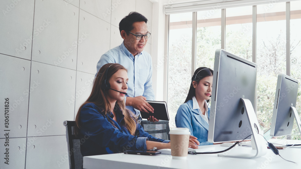 Customer support agent or call center with headset works on desktop computer while supporting the cu