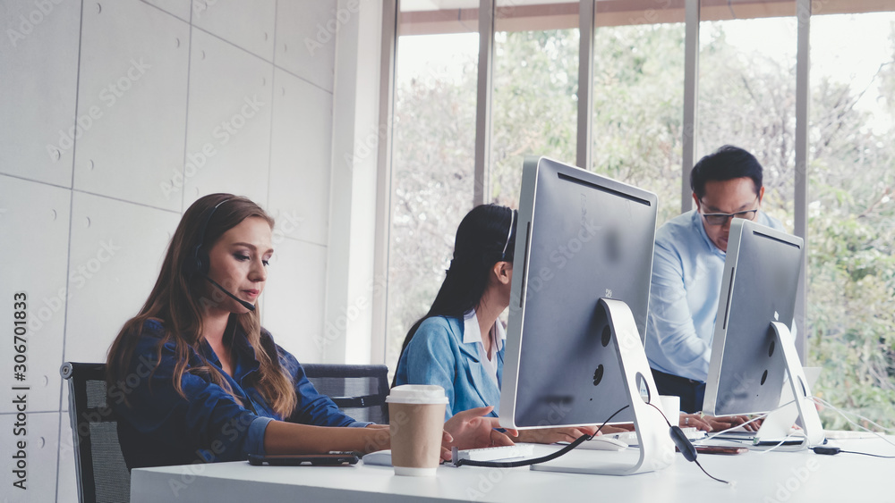 Customer support agent or call center with headset works on desktop computer while supporting the cu