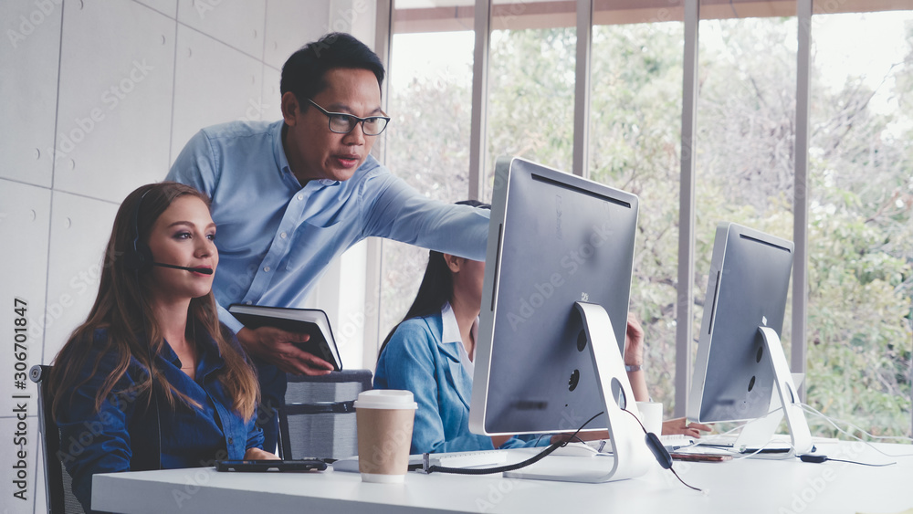 Customer support agent or call center with headset works on desktop computer while supporting the cu