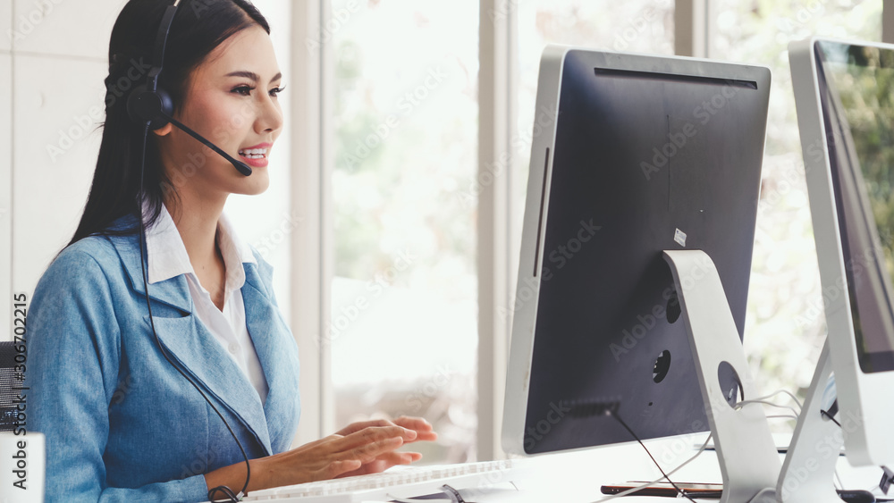 Customer support agent or call center with headset works on desktop computer while supporting the cu