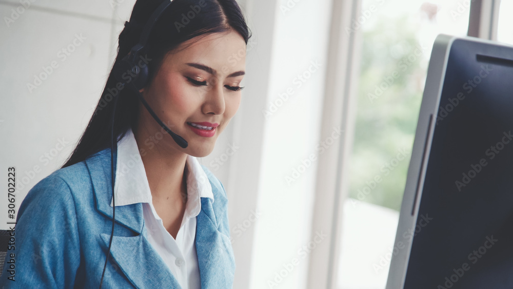 Customer support agent or call center with headset works on desktop computer while supporting the cu