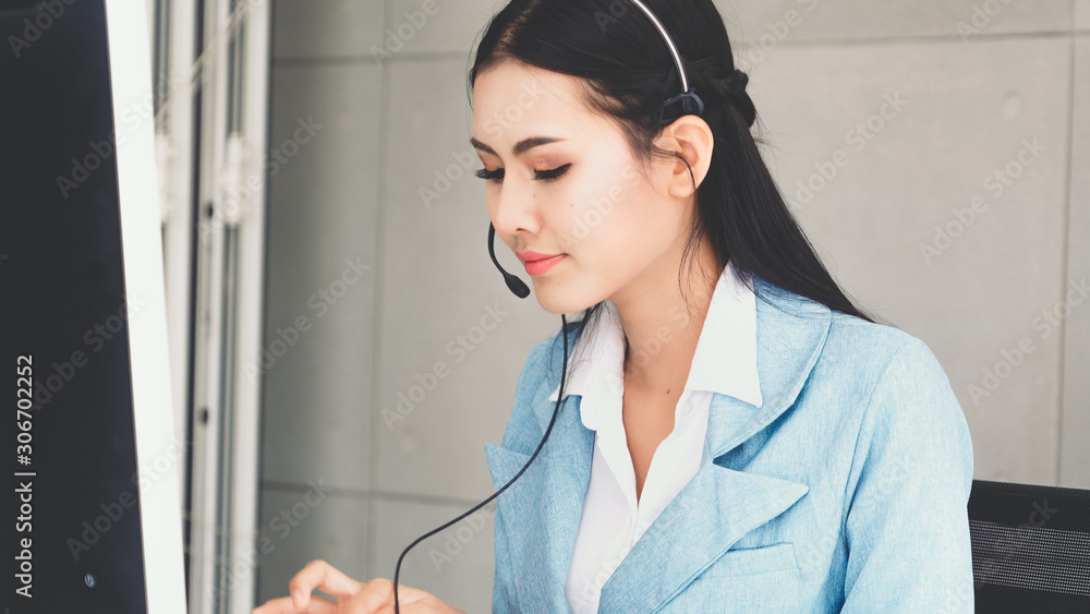 Customer support agent or call center with headset works on desktop computer while supporting the cu