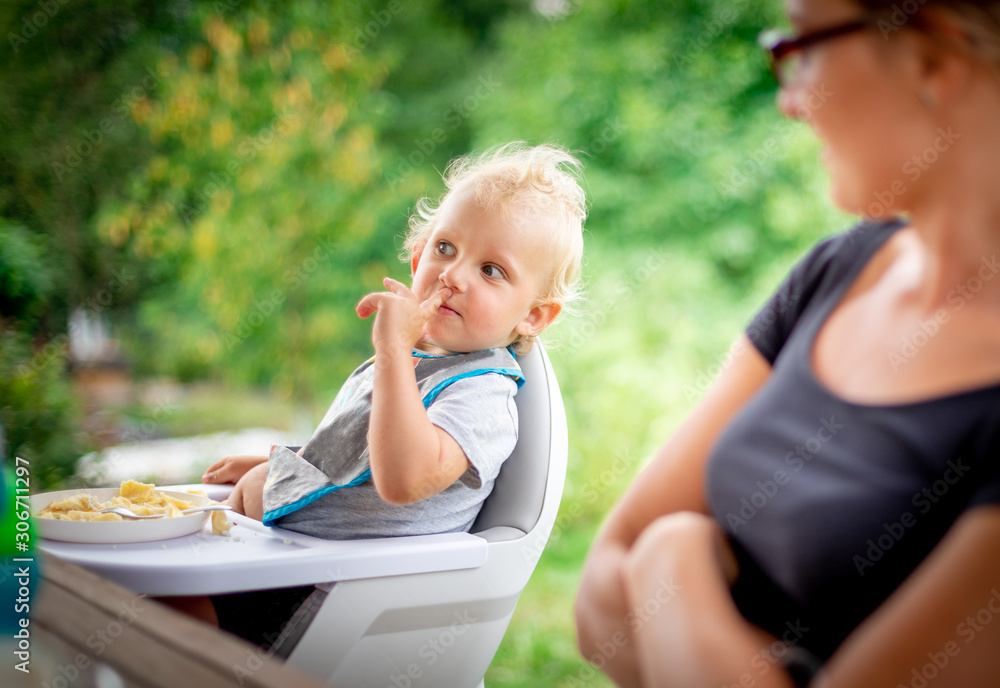 Baby sitting in high chair eating with his mom outdoor